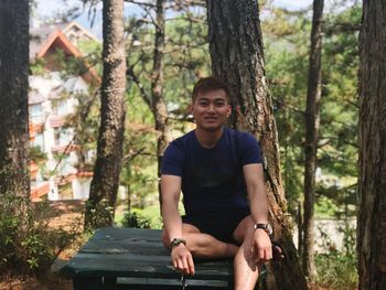 Portrait of young man sitting by tree trunk in forest
