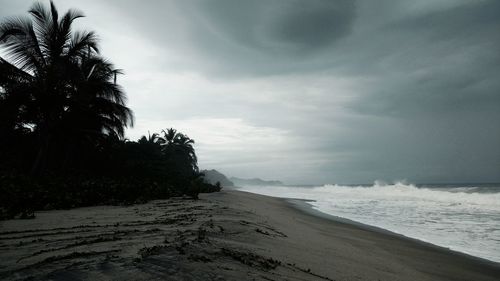 View of calm beach against cloudy sky