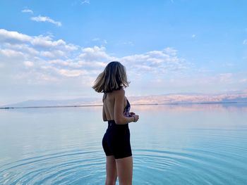 Rear view of woman standing in sea against sky