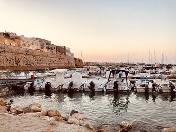 Boats moored in harbor at sunset