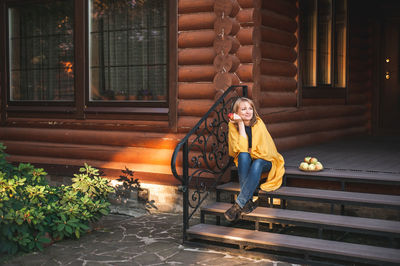 Beautiful blonde woman sits on the steps of the porch of a large wooden house. 