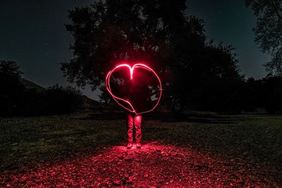 Person standing on illuminated field against sky at night