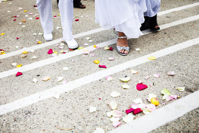Low section of bride and groom walking on rose petals at street