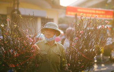 Senior man wearing hat standing by flowering plant