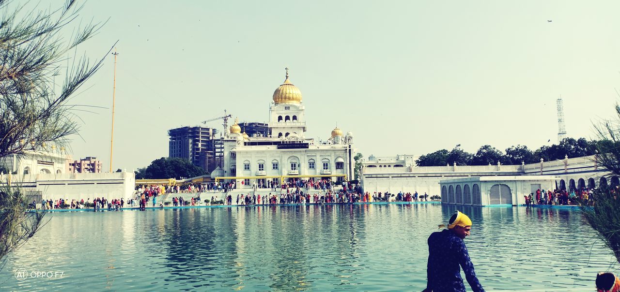 building exterior, architecture, built structure, sky, water, nature, real people, religion, travel destinations, clear sky, city, day, travel, tourism, place of worship, men, building, belief, large group of people, outdoors