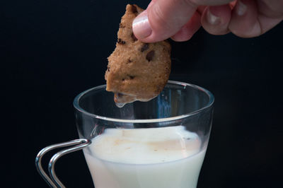 Close-up of hand holding chocolate cookie with black background