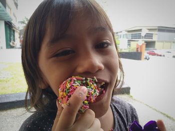 Close-up portrait of cute girl eating sweet food in city