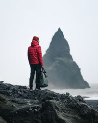 Rear view of man on rock by sea against sky