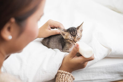 Close-up of woman feeding milk to kitten on bed at home