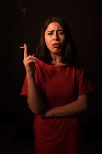 Portrait of woman holding cigarette against black background