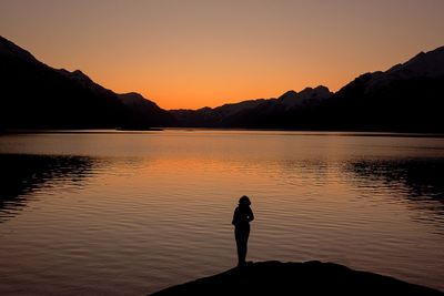 Silhouette man standing by lake against sky during sunset