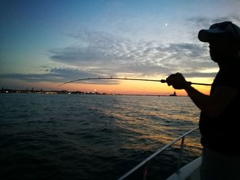 Silhouette man sailing on sea against sky during sunset