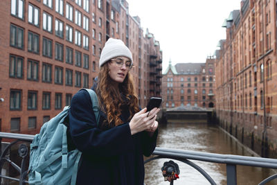 Tourist with backpack using smart phone near buildings in speicherstadt
