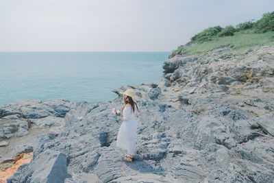 Full length of woman standing on rock by sea against sky