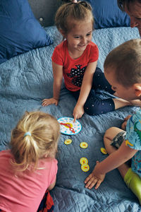 High angle view of people sitting by toy clock on bed