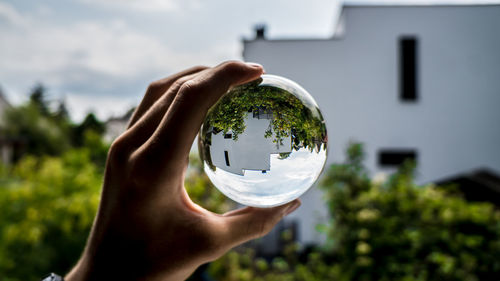 Cropped image of hand holding crystal ball against building