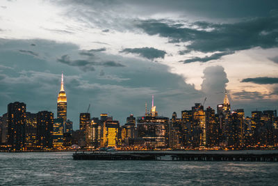 Illuminated buildings in city against cloudy sky