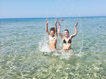 Playful female friends in bikini splashing water in sea