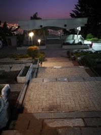 Illuminated street by building against sky at night