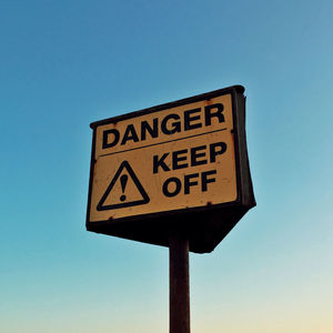 Low angle view of warning sign against blue sky