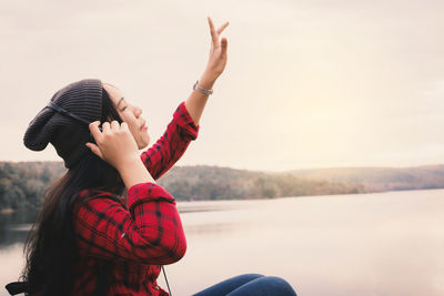 Young woman sitting by lake against clear sky