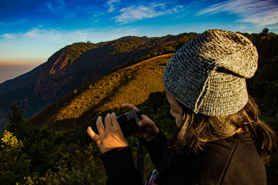 Close-up of young woman photographing while standing against mountains