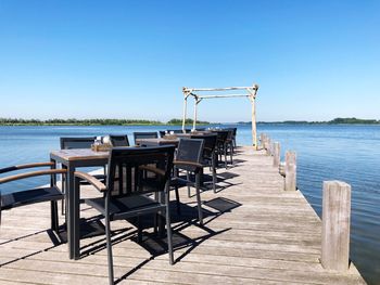 Chairs and tables on pier on sea against clear sky