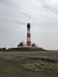 Lighthouse on field by building against sky