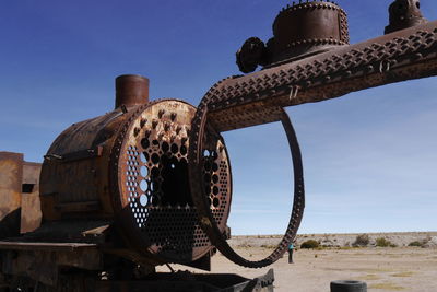 Low angle view of rusty wheel on beach against clear blue sky