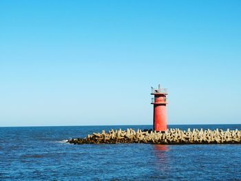 Lighthouse by sea against clear blue sky