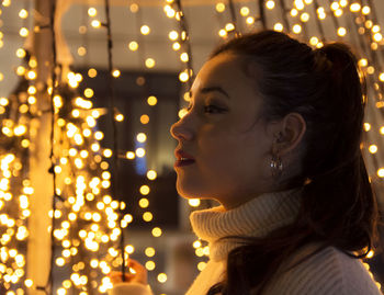 Side view of young woman against illuminated christmas lights