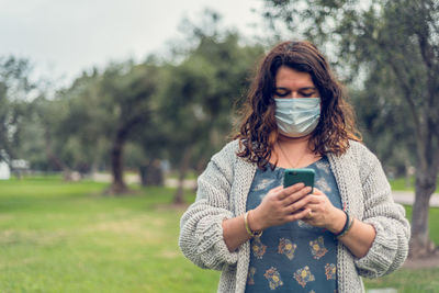 Woman wearing mask using smart phone standing in park