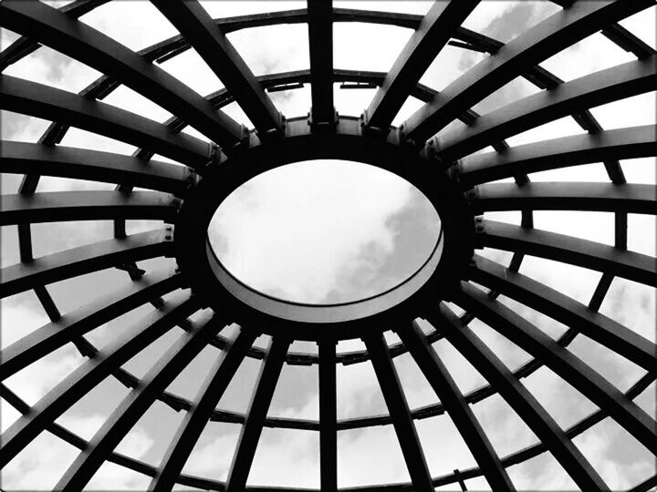 indoors, architecture, built structure, low angle view, geometric shape, ceiling, skylight, directly below, pattern, glass - material, circle, architectural feature, design, full frame, sky, transparent, backgrounds, modern, cloud - sky, shape