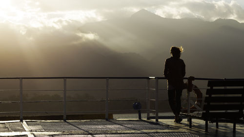 Rear view of woman standing by railing against sea