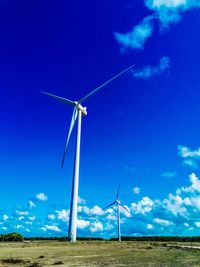 Low angle view of wind turbines on field against blue sky