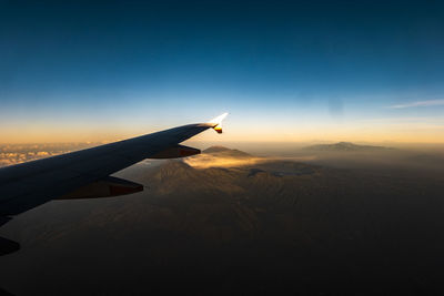 Airplane flying over landscape against sky during sunset