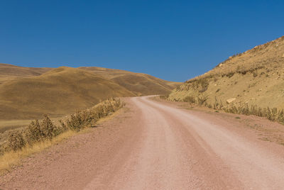 Dirt road amidst desert against clear blue sky