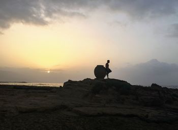 Silhouette man on rock against sky during sunset