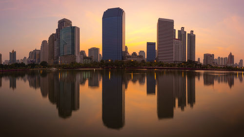 Scenic view of lake by cityscape against sky during sunset