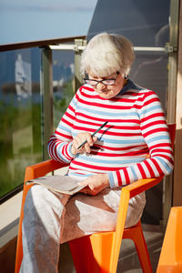 Elderly woman in glasses sitting on balcony near the sea