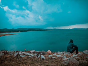 Rear view of man sitting on rock against blue sky