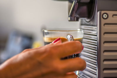 Close-up of barista hand holding coffee cup by machine in cafe