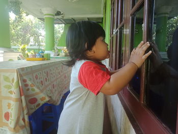 Side view of woman looking through window