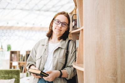 Young brunette teenager girl student in glasses with mobile phone at modern library, public place