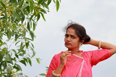 Portrait of woman holding sunglasses against sky