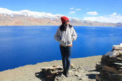 Full length of woman standing on lakeshore against mountains on sunny day