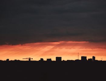 Silhouette of buildings against cloudy sky at sunset