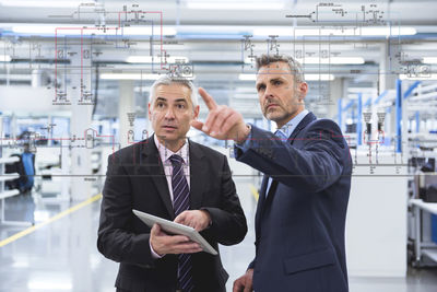 Two businessmen looking at graphic on glass pane in factory hall