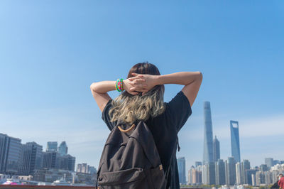 Rear view of woman against cityscape against blue sky