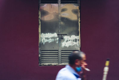 Reflection of man photographing on mobile phone while standing on window